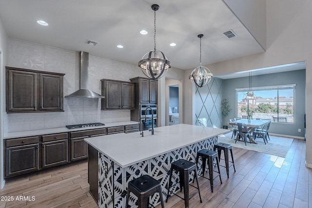 22771 N 98th Dr, Peoria, AZ 85383 - kitchen featuring a chandelier, wall chimney range hood, gas stovetop, light countertops, and a breakfast bar