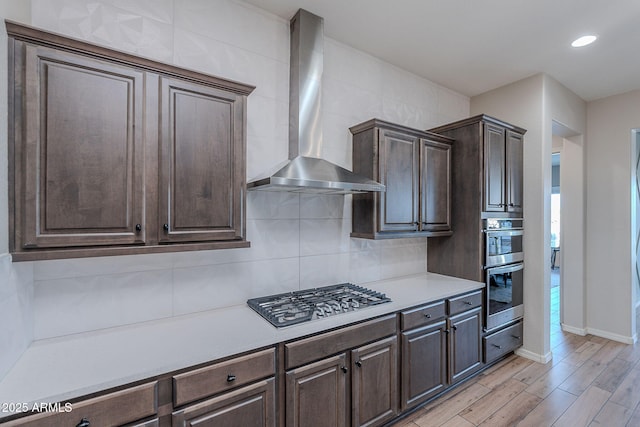 22771 N 98th Dr, Peoria, AZ 85383 - kitchen with wall chimney range hood, stainless steel appliances, dark brown cabinets, light countertops, and light wood-style floors
