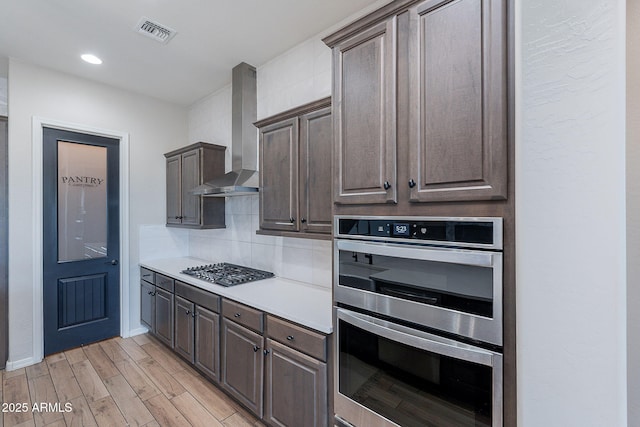 22771 N 98th Dr, Peoria, AZ 85383 - kitchen featuring wall chimney range hood, appliances with stainless steel finishes, light wood-style floors, backsplash, and light countertops