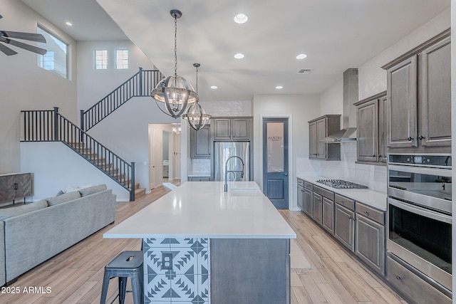 22771 N 98th Dr, Peoria, AZ 85383 - kitchen featuring wall chimney exhaust hood, appliances with stainless steel finishes, open floor plan, a breakfast bar, and light wood-style flooring