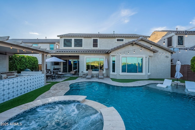 22771 N 98th Dr, Peoria, AZ 85383 - back of property featuring stucco siding, an outdoor kitchen, a tile roof, outdoor dining area, and a pool with connected hot tub