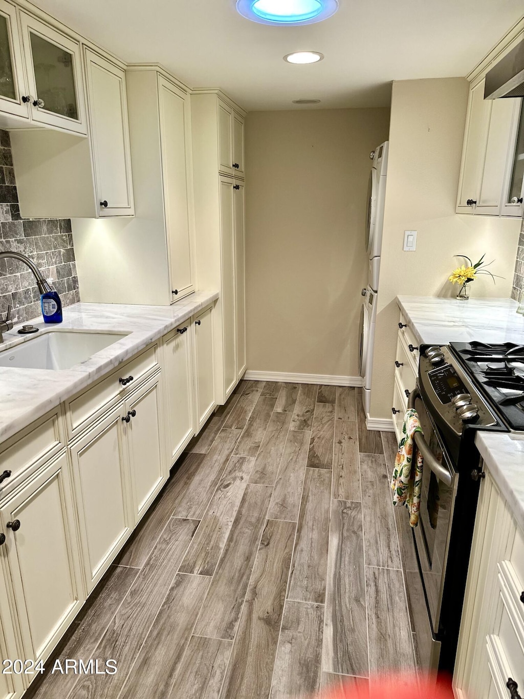 kitchen with light stone countertops, sink, backsplash, stainless steel range with gas stovetop, and light wood-type flooring