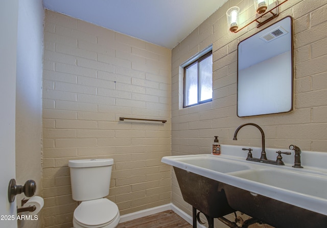 bathroom with brick wall, sink, hardwood / wood-style floors, and toilet