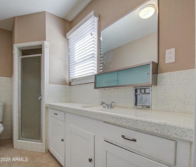 bathroom with a shower with door, tile walls, tile patterned flooring, vanity, and toilet