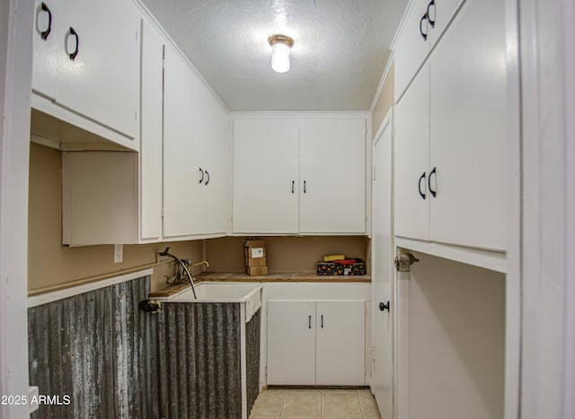 clothes washing area with sink, light tile patterned floors, and a textured ceiling