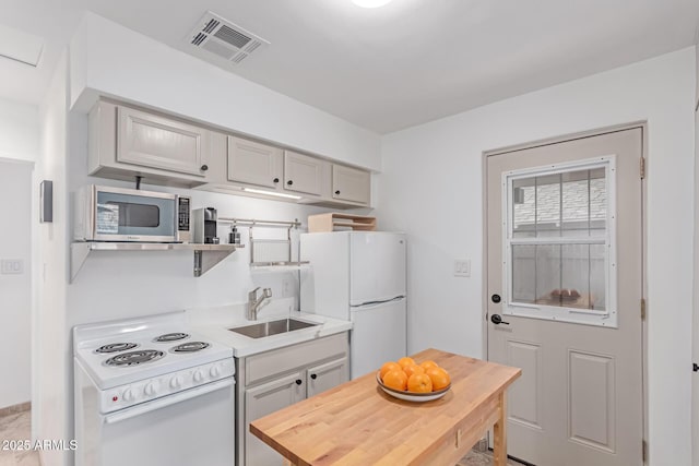 kitchen with a sink, gray cabinets, white appliances, and visible vents