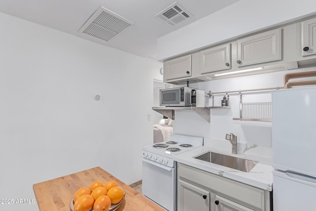 kitchen with visible vents, a sink, gray cabinets, and white appliances