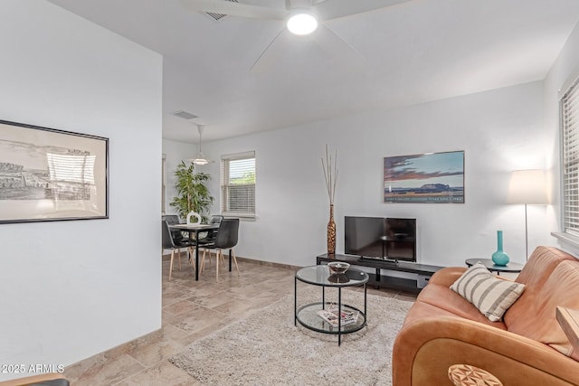 living area with a ceiling fan, baseboards, stone finish flooring, and visible vents