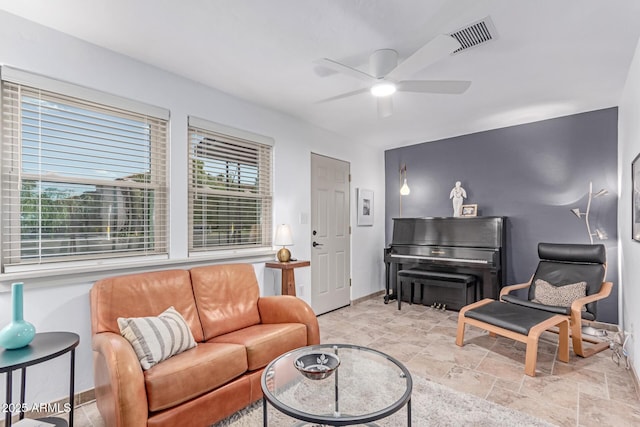 living room featuring stone finish floor, baseboards, a ceiling fan, and visible vents