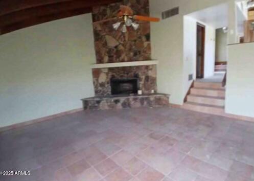 unfurnished living room with visible vents, a stone fireplace, and a ceiling fan