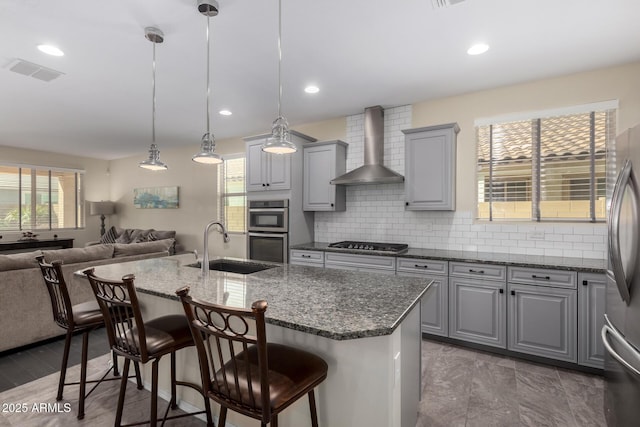 kitchen featuring pendant lighting, sink, a kitchen breakfast bar, a kitchen island with sink, and wall chimney exhaust hood