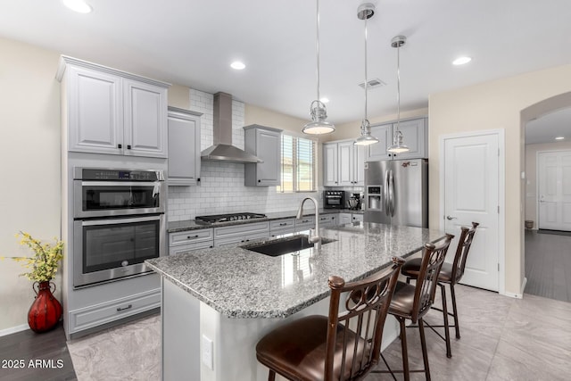 kitchen featuring appliances with stainless steel finishes, sink, a kitchen island with sink, and wall chimney exhaust hood