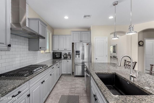 kitchen featuring gray cabinets, sink, dark stone countertops, stainless steel appliances, and wall chimney exhaust hood