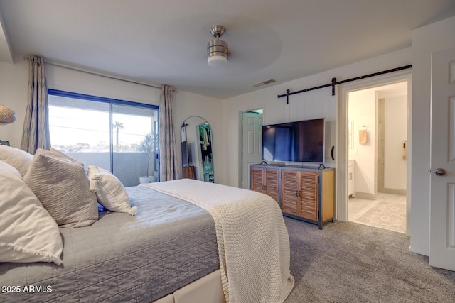 bedroom featuring ceiling fan, ensuite bathroom, a barn door, and carpet