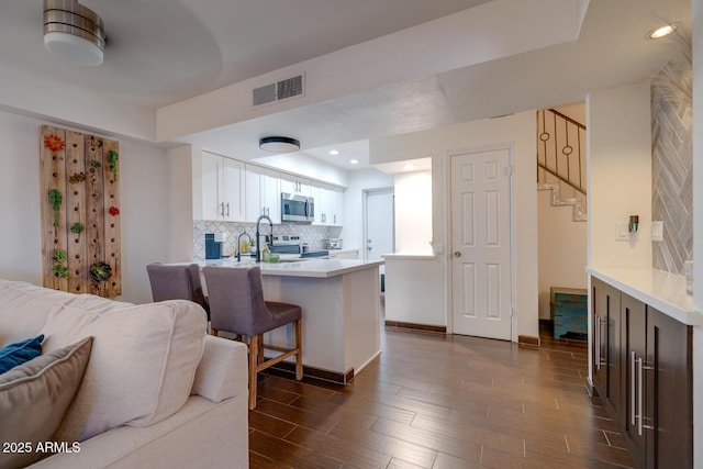 kitchen featuring white cabinetry, tasteful backsplash, appliances with stainless steel finishes, a kitchen breakfast bar, and kitchen peninsula