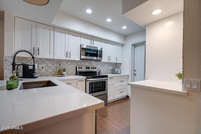 kitchen featuring backsplash, kitchen peninsula, white cabinets, and appliances with stainless steel finishes