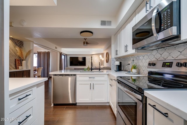 kitchen with sink, white cabinets, decorative backsplash, kitchen peninsula, and stainless steel appliances