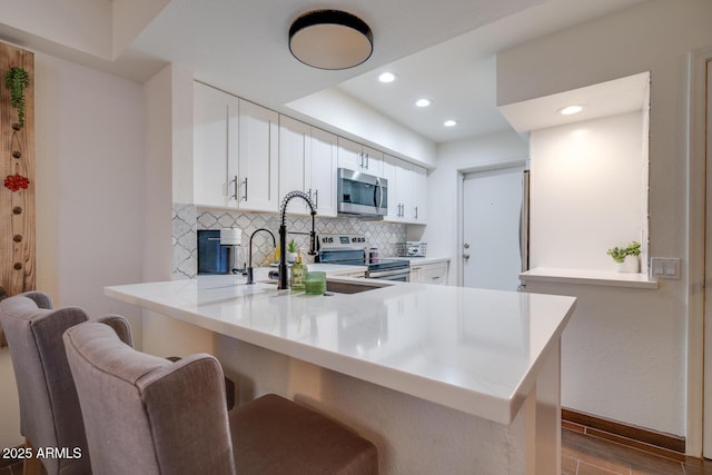 kitchen with white cabinetry, tasteful backsplash, a kitchen breakfast bar, kitchen peninsula, and stainless steel appliances