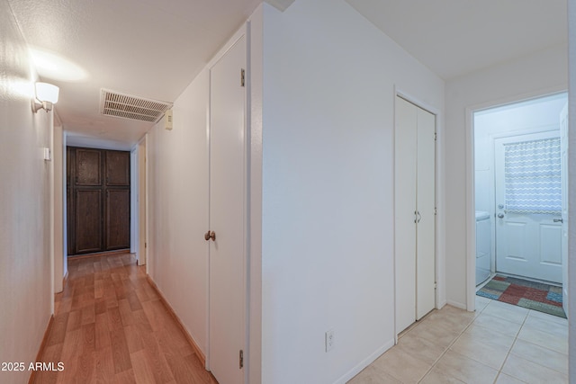 hallway with light wood finished floors, visible vents, and washer / clothes dryer