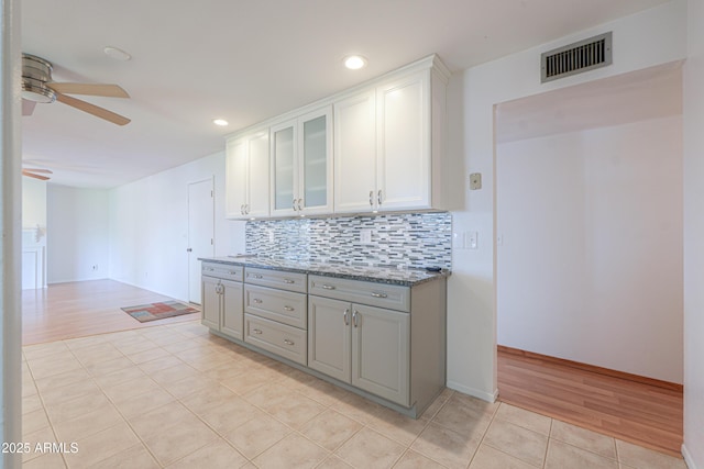kitchen featuring light tile patterned floors, decorative backsplash, glass insert cabinets, visible vents, and ceiling fan