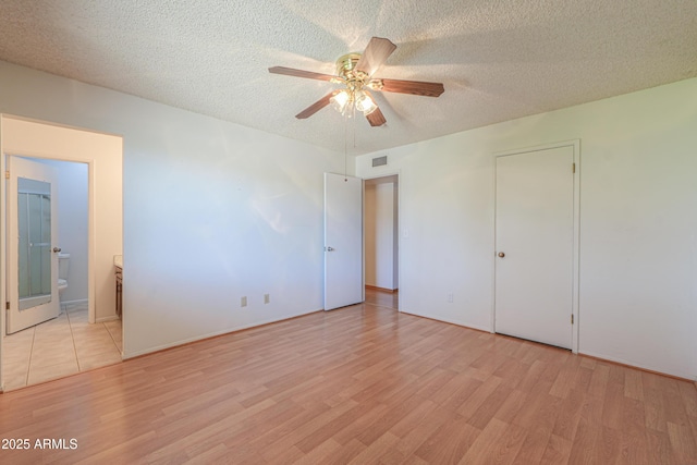 unfurnished bedroom featuring a textured ceiling, light wood-style floors, visible vents, a ceiling fan, and ensuite bath