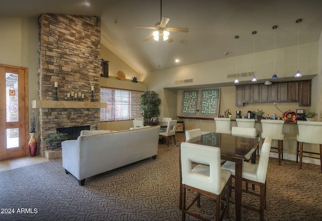 carpeted dining space with ceiling fan, a stone fireplace, and high vaulted ceiling