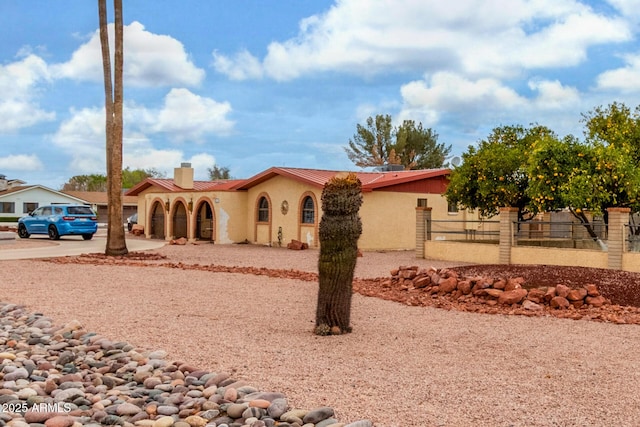 mediterranean / spanish-style house featuring stucco siding, driveway, a chimney, and fence