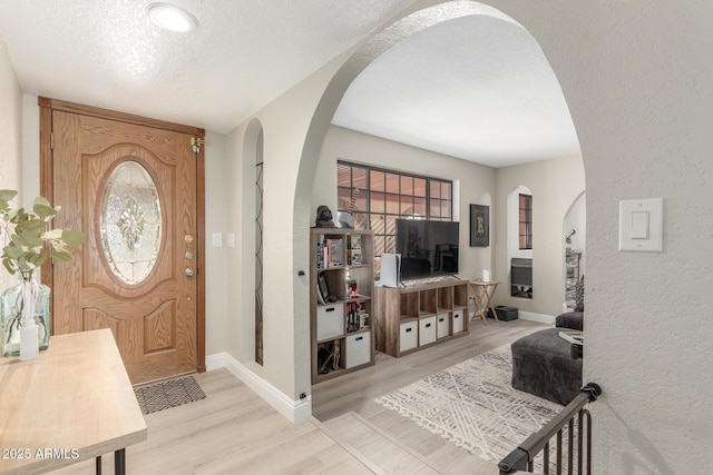 foyer with arched walkways, a textured ceiling, a textured wall, and wood finished floors