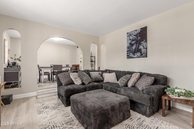 living area with light wood-style flooring, baseboards, and arched walkways