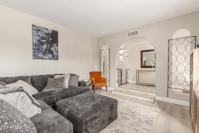 living room featuring visible vents, arched walkways, baseboards, and wood finished floors