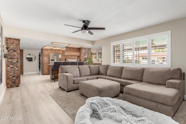 living area with baseboards, light wood-style flooring, a textured ceiling, and ceiling fan