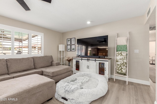 living room with visible vents, baseboards, ceiling fan, and light wood finished floors