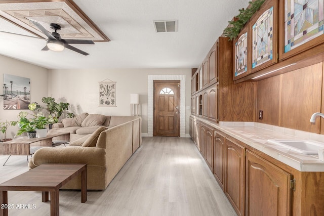 living room with visible vents, light wood-style flooring, and a ceiling fan