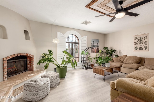 living room with visible vents, ceiling fan, a fireplace, wood finished floors, and a textured ceiling