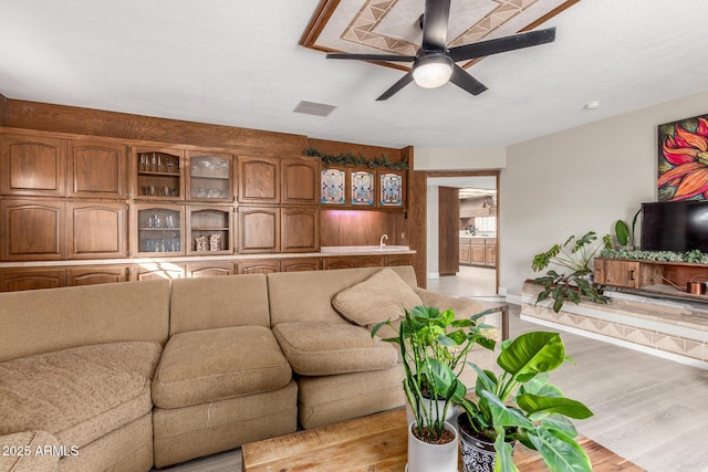 living room with visible vents, wet bar, light wood-type flooring, and ceiling fan