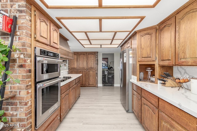 kitchen with light wood finished floors, brown cabinets, stainless steel appliances, and backsplash