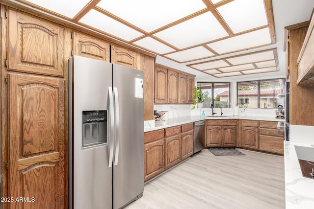 kitchen featuring light wood-type flooring, light countertops, brown cabinetry, stainless steel appliances, and a sink