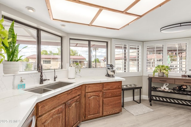 kitchen featuring a sink, light wood-type flooring, plenty of natural light, and brown cabinets