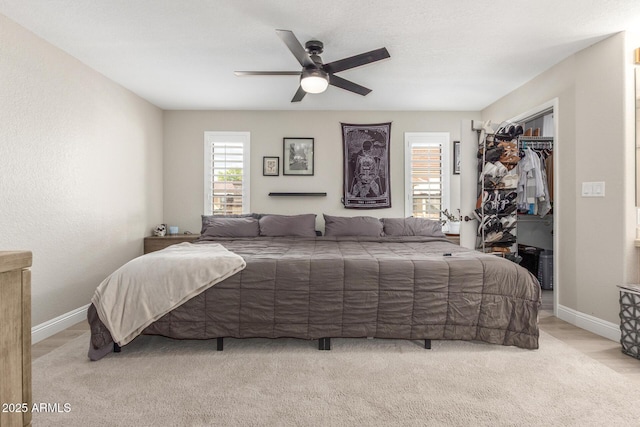 bedroom featuring a walk in closet, baseboards, a closet, and ceiling fan