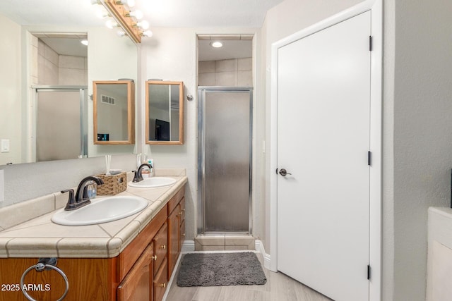 full bathroom with double vanity, a stall shower, and a sink