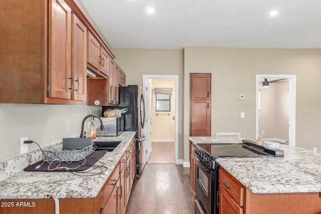 kitchen with light stone counters, brown cabinets, a center island, and black range with electric stovetop