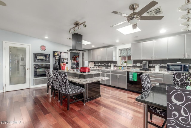 kitchen featuring visible vents, black appliances, a kitchen breakfast bar, tasteful backsplash, and island range hood