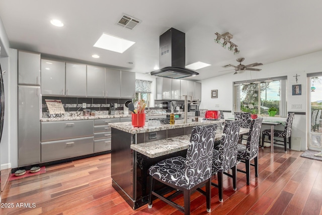 kitchen featuring light wood-style floors, a breakfast bar area, island exhaust hood, and visible vents