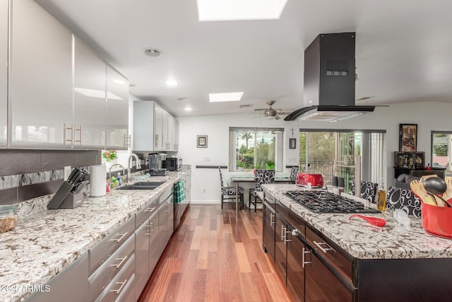 kitchen with a sink, light wood-style floors, vaulted ceiling with skylight, and extractor fan