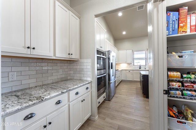 kitchen with white cabinets, backsplash, light stone countertops, and stainless steel appliances