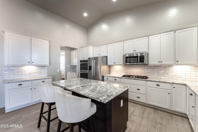 kitchen with high vaulted ceiling, a kitchen breakfast bar, white cabinetry, and stainless steel appliances