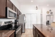 kitchen featuring black range, light tile patterned floors, dark brown cabinetry, and dark stone counters