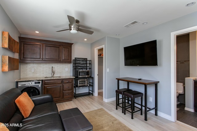 living room with visible vents, light wood finished floors, washer / dryer, and a ceiling fan