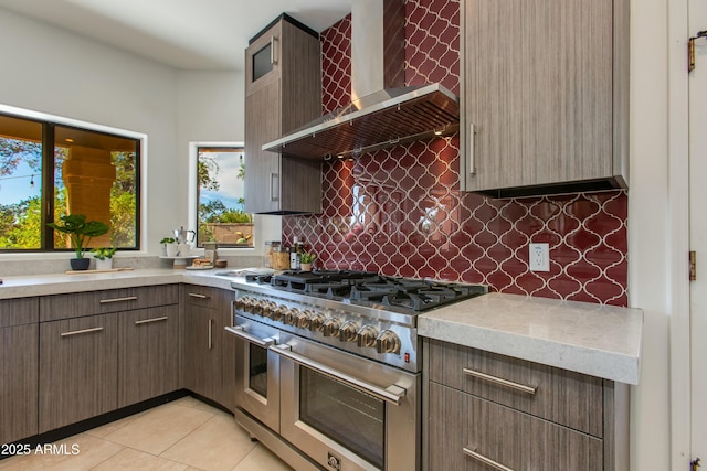 kitchen featuring light tile patterned floors, tasteful backsplash, range with two ovens, light countertops, and wall chimney range hood