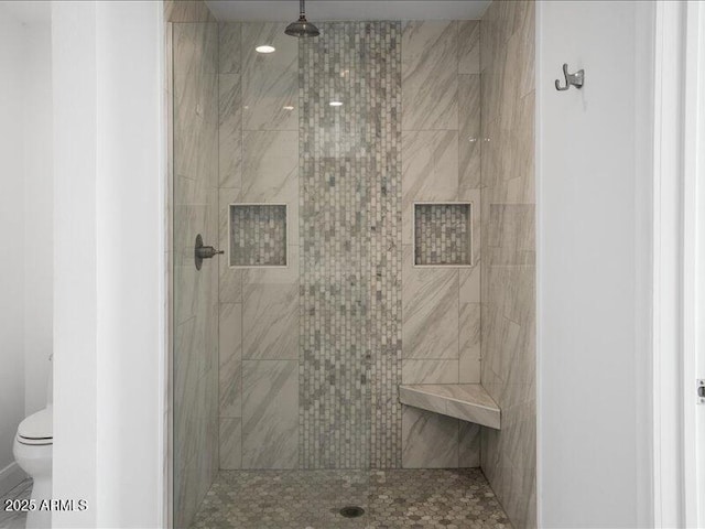 bathroom with a tile shower and toilet